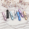 A collection of portable refillable perfume bottles in various metallic colors arranged on a white marble surface.