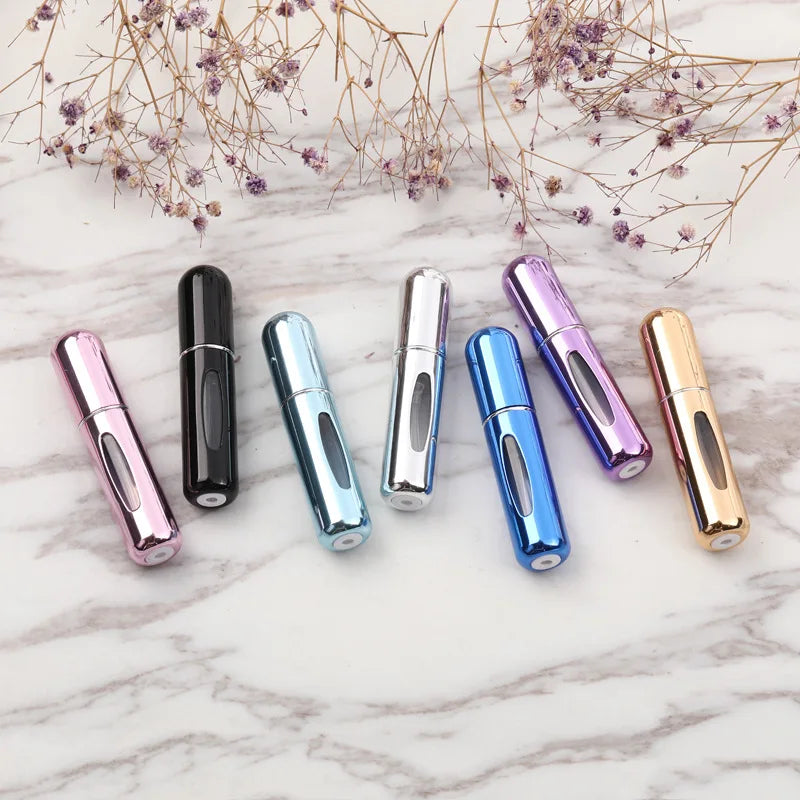 A collection of portable refillable perfume bottles in various metallic colors arranged on a white marble surface.