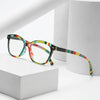 Retro cat eye reading glasses with multicolored frames resting on a white box.