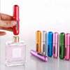 A hand holds a red perfume refill spray, next to several metallic colored mini perfume bottles.