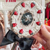 A decorative makeup mirror set with a silver frame and a black ribbon bow, featuring a framed design.