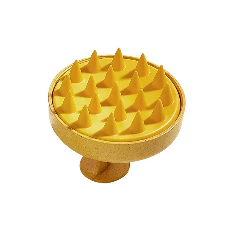 A yellow silicone scalp massage brush with pointed tips resting on a round wooden base.