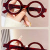 A pair of round, reddish-brown acetate reading glasses with a tortoiseshell pattern being held by a hand.
