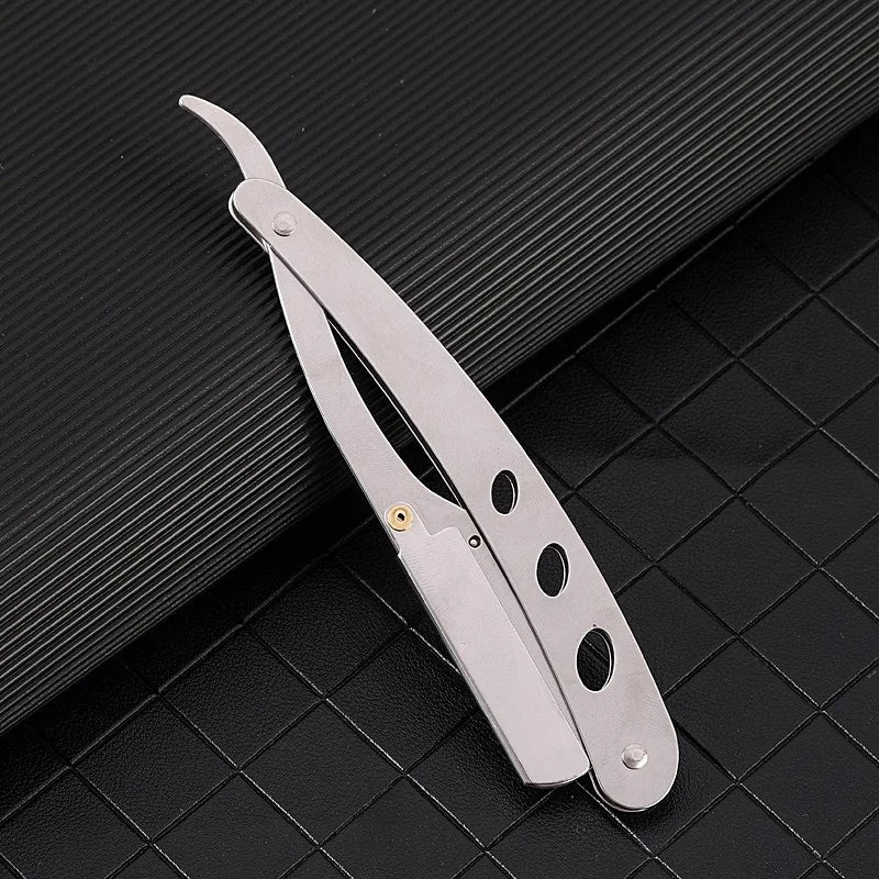 A silver manual straight edge shaver kit lying on a dark textured surface.