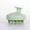 A light green silicone body and scalp massage brush with a wide head and multiple pointed bristles.