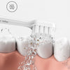 A white sonic electric toothbrush is shown cleaning teeth in a pink bowl, with water splashing.