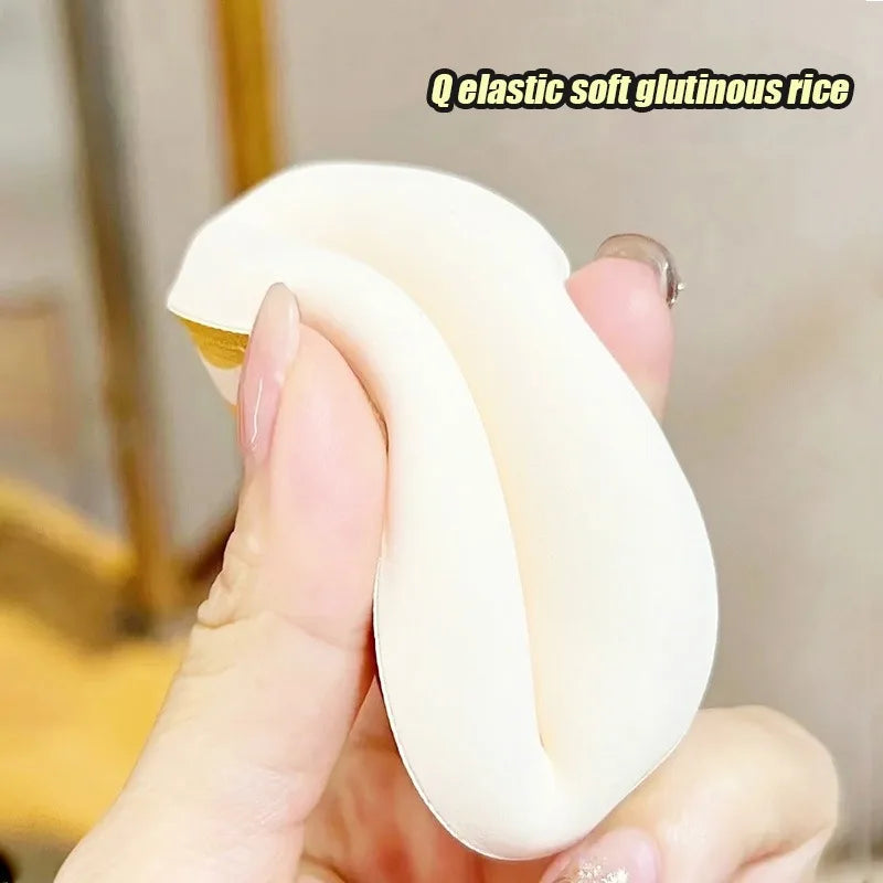 A hand holds a white elastic soft glutinous rice makeup puff, showing its shape and texture.