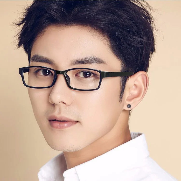 A close-up portrait of a man wearing black rectangular reading glasses against a light background.