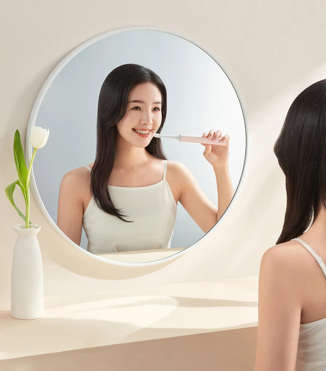 A woman smiles while using a white sonic electric toothbrush with dual cleaning modes in a round mirror.
