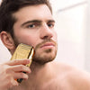 A man is holding a gold-colored electric shaver kit near his face.
