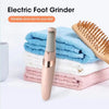 A pink electric foot grinder is shown next to a stack of white, pink, and blue towels and a wooden brush for exfoliating feet