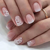 A close-up of a hand displaying press-on acrylic nails decorated with delicate white floral designs.