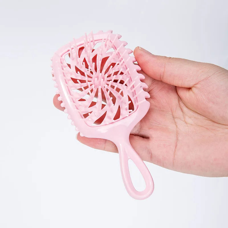 A hand holds a pink detangling hair comb with a wide, serrated mesh for styling or detangling.