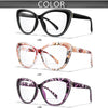 A display of three pairs of clear cateye reading glasses in black, pink floral pattern, and purple leopard print.