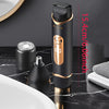 A black electric body hair trimmer with a gold accent is shown next to its detachable head and on a marble surface.