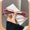 A pair of pink cat eye reading glasses with a dark frame resting on a white card, held by a hand.