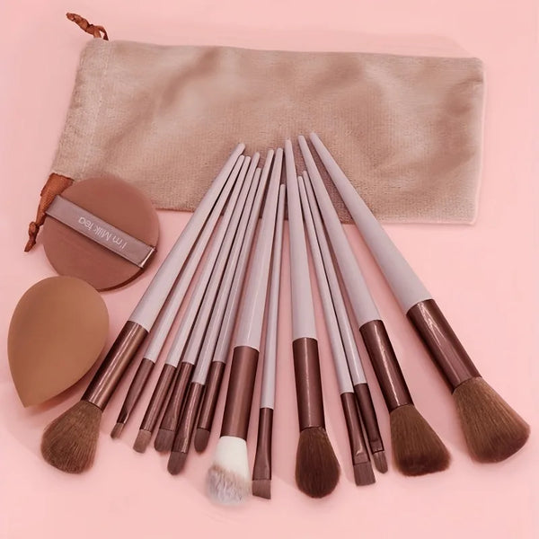 A collection of fifteen makeup brushes with wooden handles and synthetic bristles displayed on a pink background.