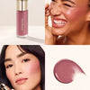 A cosmetic product featuring a pink liquid blush stick and a swatch of soft pink liquid blush on skin.