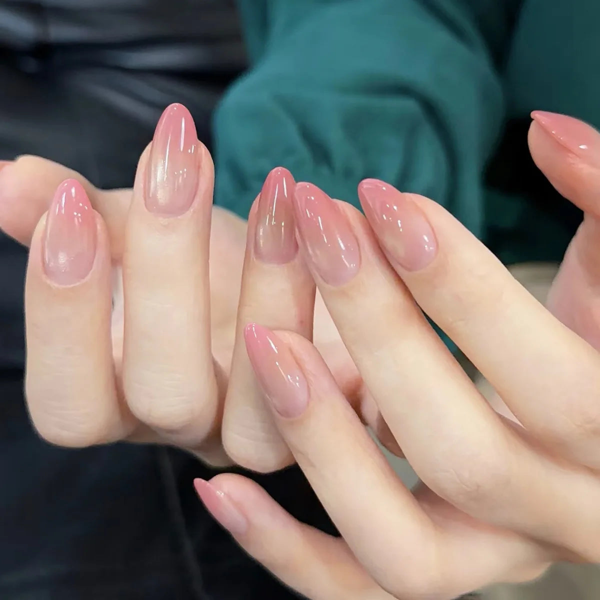 Gros plan de mains montrant un ensemble de faux ongles à almonds roses français sur les doigts.