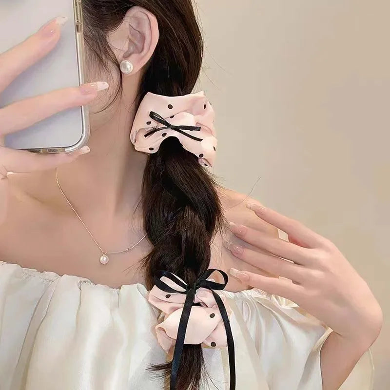 Une femme porte des élastiques pour cheveux en satin à pois roses et un haut blanc, ses cheveux sont coiffés en tresse longue