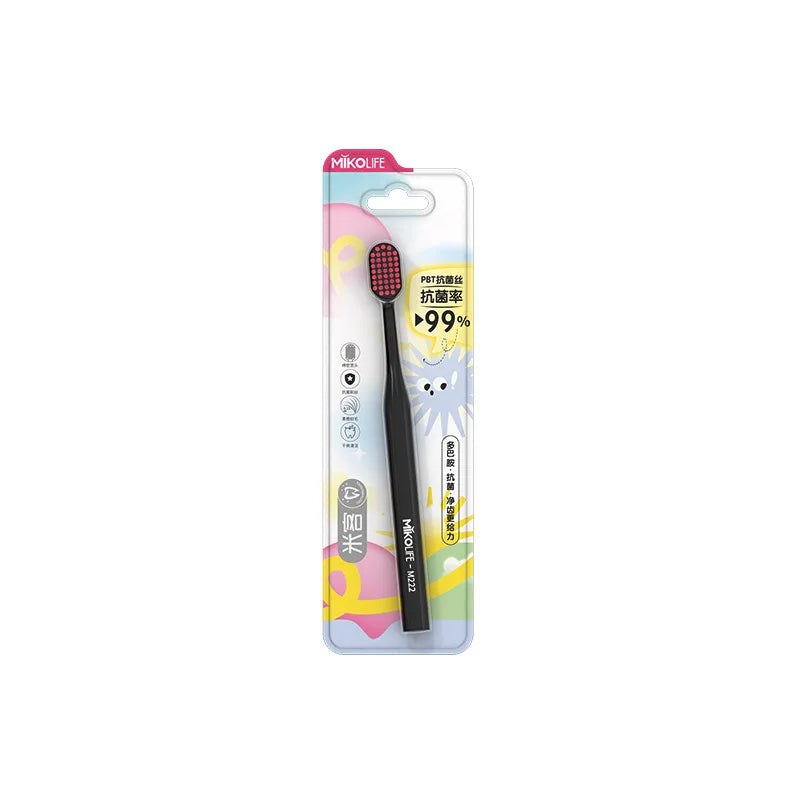 A package of a black soft bristle manual toothbrush for adults with a yellow and pink design.