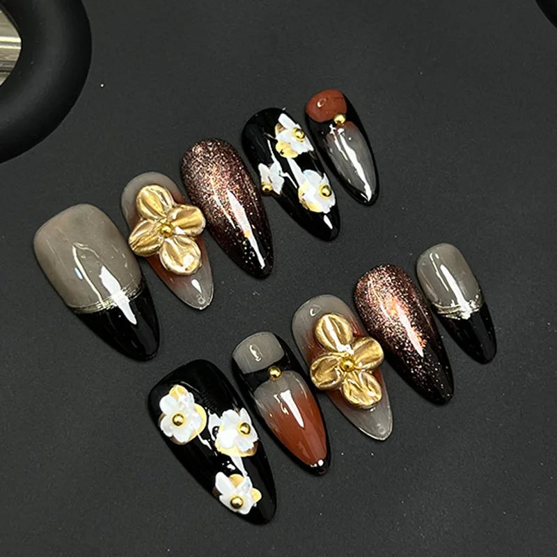 Colección de uñas postizas negras y nude con diseños de pétalo almendra tallados a mano y acentos dorados.