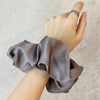 Une main porte un tissu de mousseline de satin gris attaché autour du poignet, suggérant des élastiques pour cheveux élégants