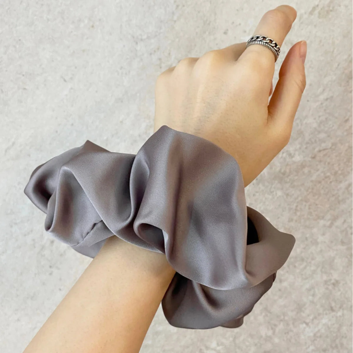 Une main porte un tissu de mousseline de satin gris attaché autour du poignet, suggérant des élastiques pour cheveux élégants
