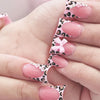 Nude pink press-on nails with leopard print and 3D charms displayed on a hand.