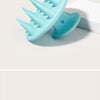 Brosse de massage pour le cuir chevelu en silicone bleu clair avec des poils pointus, sur une surface blanche.
