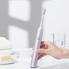 A hand holds a purple sonic electric toothbrush with blue bristles, resting on a white surface.