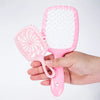 A hand holds a pink detangling hair comb with white bristles against a white background.