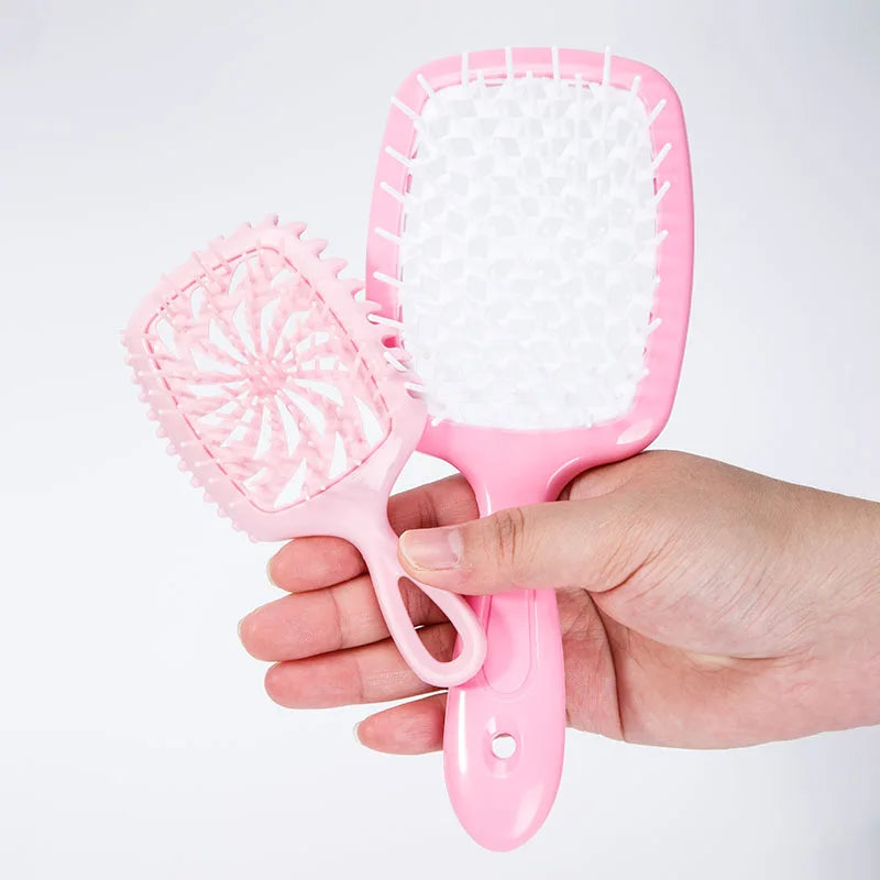 A hand holds a pink detangling hair comb with white bristles against a white background.