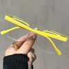 Una mano sostiene unas gafas de lectura cuadradas amarillas anti-luz azul con monturas transparentes sobre un fondo gris.