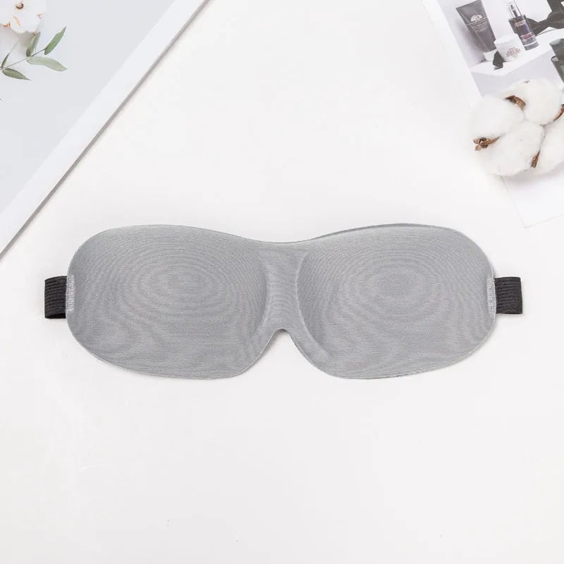 A gray 3D sleep mask is shown lying on a white surface.
