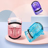 A set of mini folding eyelash curlers in pink and blue plastic are displayed on a light surface.