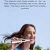 A woman is using a portable, cordless ultrasonic tooth cleaner on her teeth outdoors.