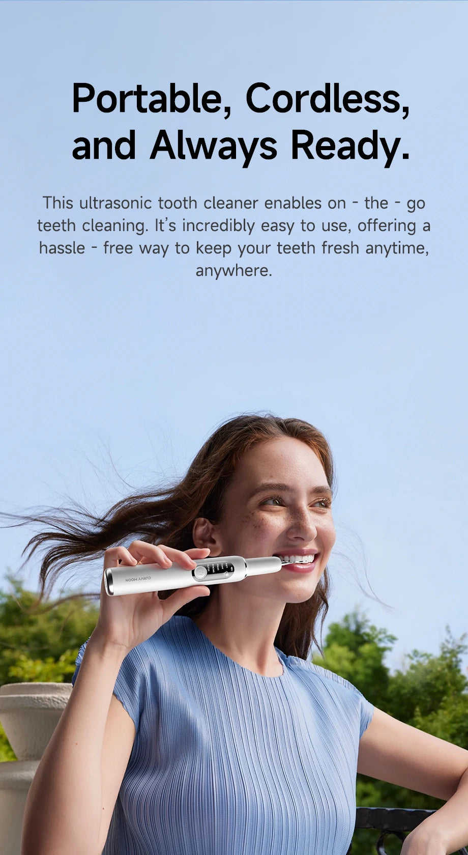 A woman is using a portable, cordless ultrasonic tooth cleaner on her teeth outdoors.