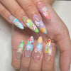 A hand displaying a set of press-on nails featuring pink flowers and stars on a light pink background.