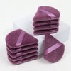 A stack of triangular cosmetic powder puffs in a dusty purple velvet fabric with satin ribbon accents.
