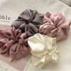Collection de pinces à cheveux en mousseline satinées dans les tons mauve, gris et crème, arrangées sur une surface blanche.