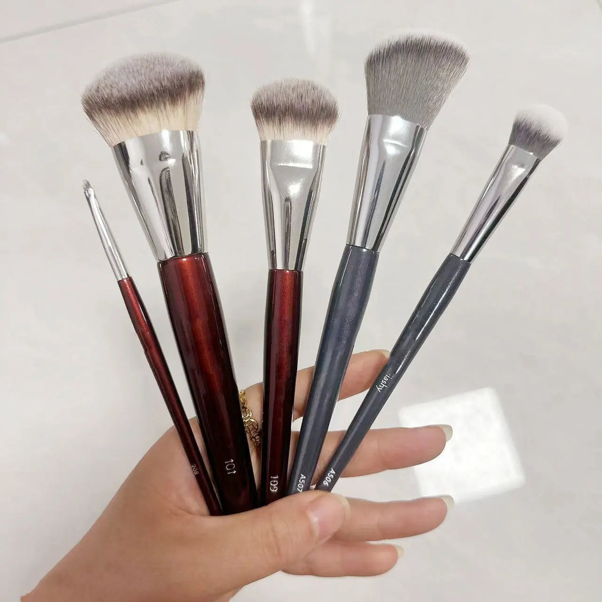 A hand holds a set of five makeup brushes with varying sizes and colors for sculpting and application.