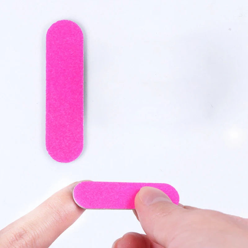 A hand is holding a bright pink, oval-shaped double-sided mini nail file.