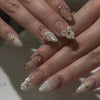 Close-up of a hand displaying pink flower press on nails with gold accents.