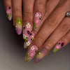 Close-up of a hand displaying pink and green press-on false nails decorated with white flowers and black ladybugs