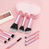 A pink makeup brush set with ten brushes and a matching compact case is displayed on a light pink background.