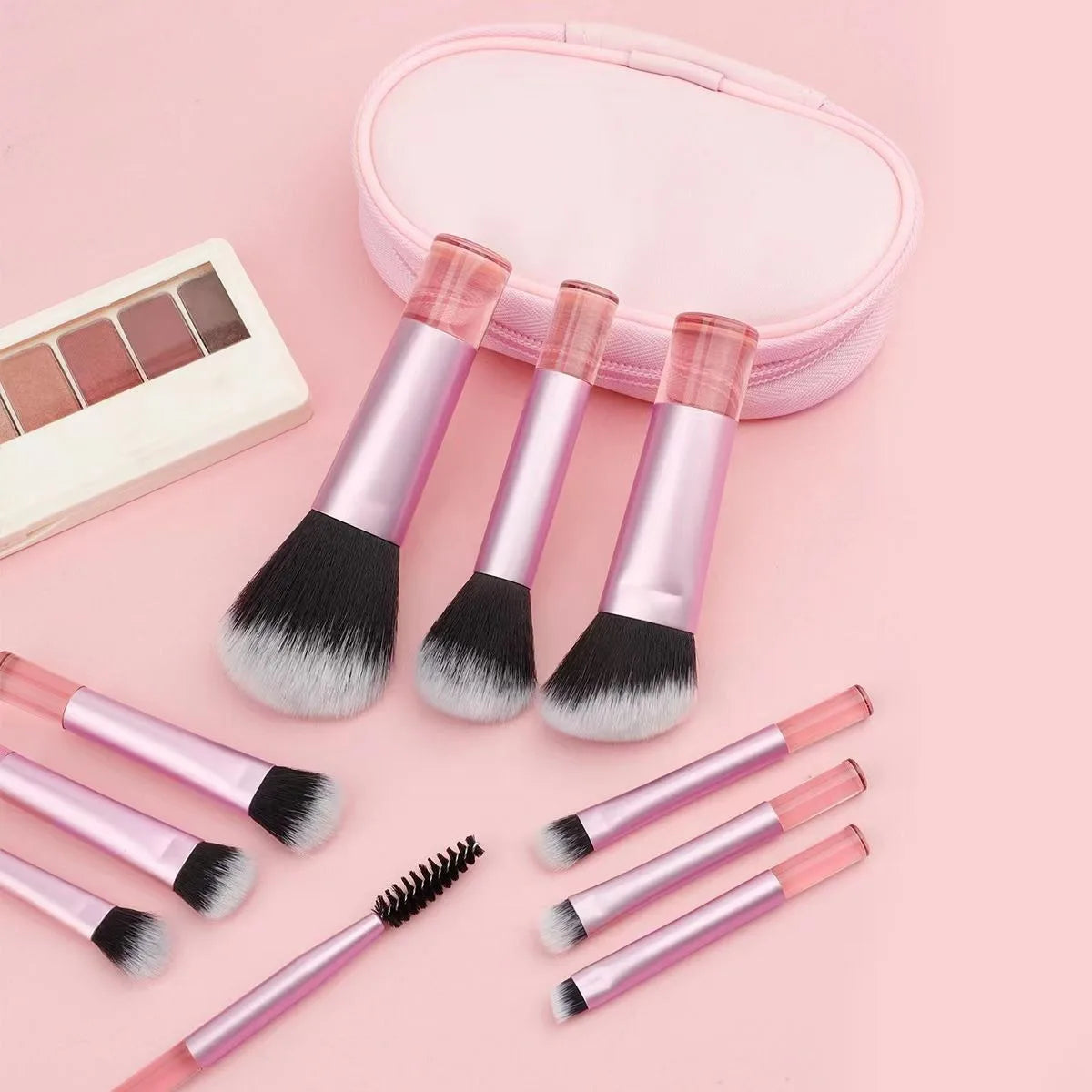 A pink makeup brush set with ten brushes and a matching compact case is displayed on a light pink background.