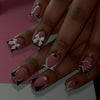 A hand displaying nude pink press-on nails decorated with black and white leopard print and 3D charms.