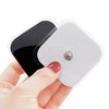 A hand holds a white electrode pad with a black section, showing the size and shape of the muscle stimulator pads.