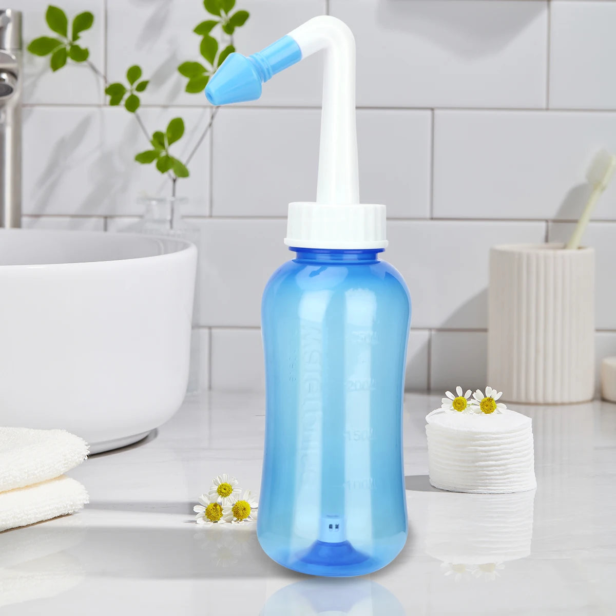 A light blue nasal irrigation bottle with a white nozzle is shown on a white countertop next to a sink and some cotton pads.